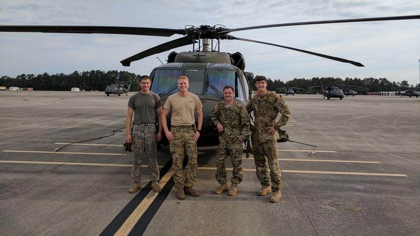 Four people in army clothes standing in front of a helicopter on a landing pad