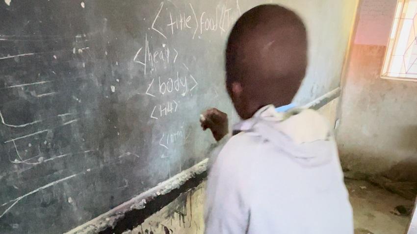 Child at a blackboard in a classroom in Kenya writing HTML code