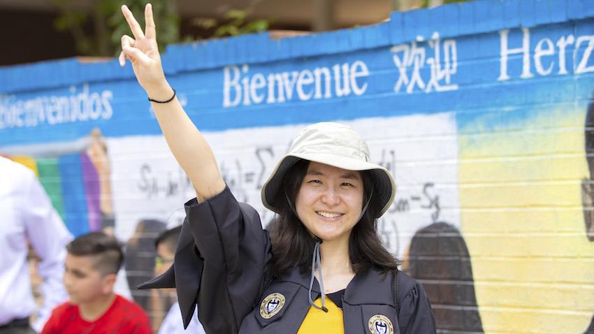 Georgia Tech graduate in graduation robe and bucket hat giving a peace sign