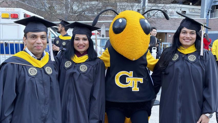 Three graduates wearing graduation regalia and posing with Buzz