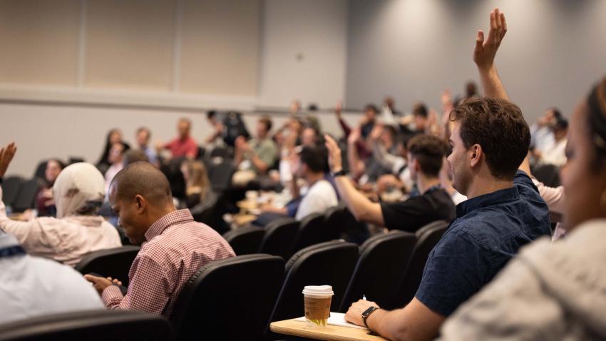 Audience in auditorium at OMSCS Conference, with people raising their hands to ask questions