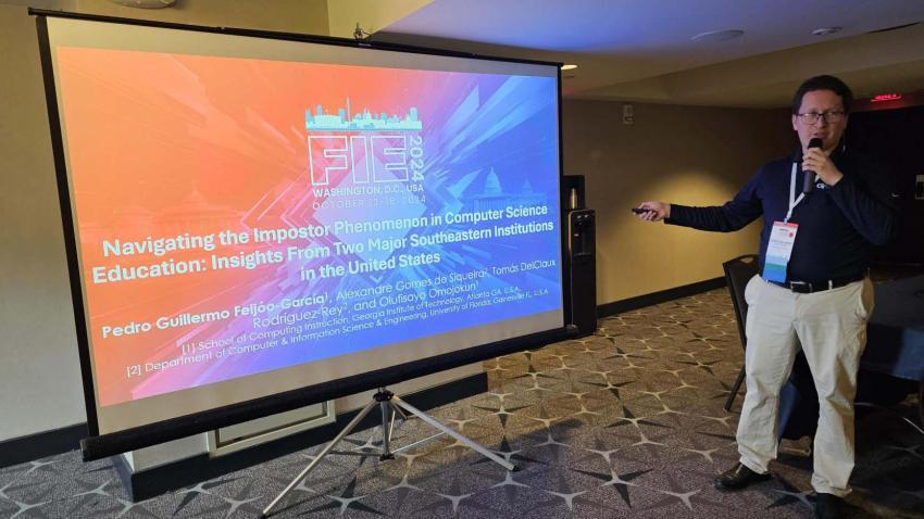 Feijoo Garcia talking into a microphone and pointing at a presentation screen