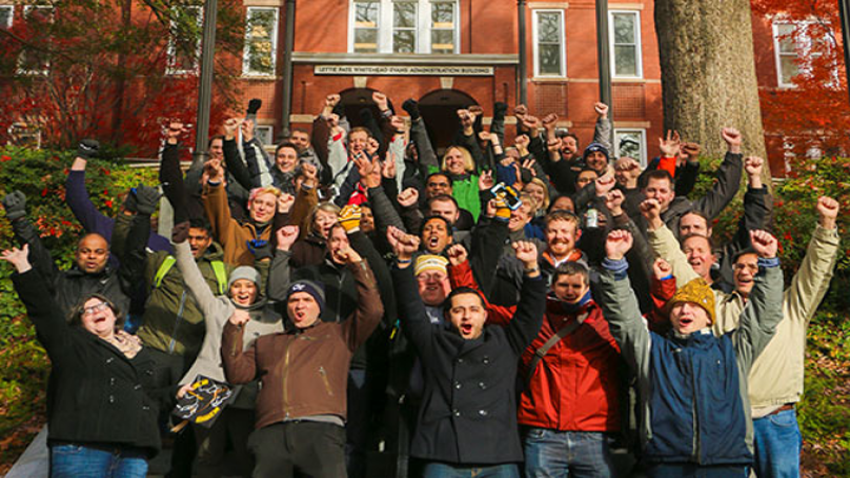 Students and alumni standing in front of Georgia Tech's tower building, raising their fists in the air and cheering