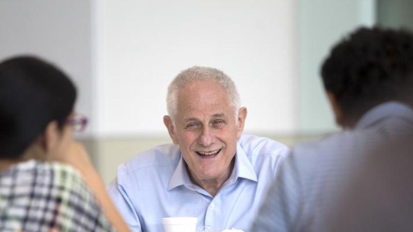 Zvi Galil in a light blue button-up shirt, seated and laughing