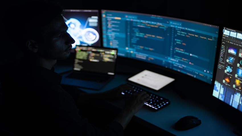 Person in a dark room looking at multiple computer monitors