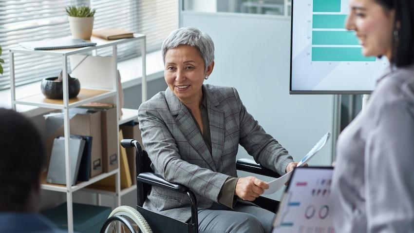 Woman in wheelchair in an office talking to 2 other people