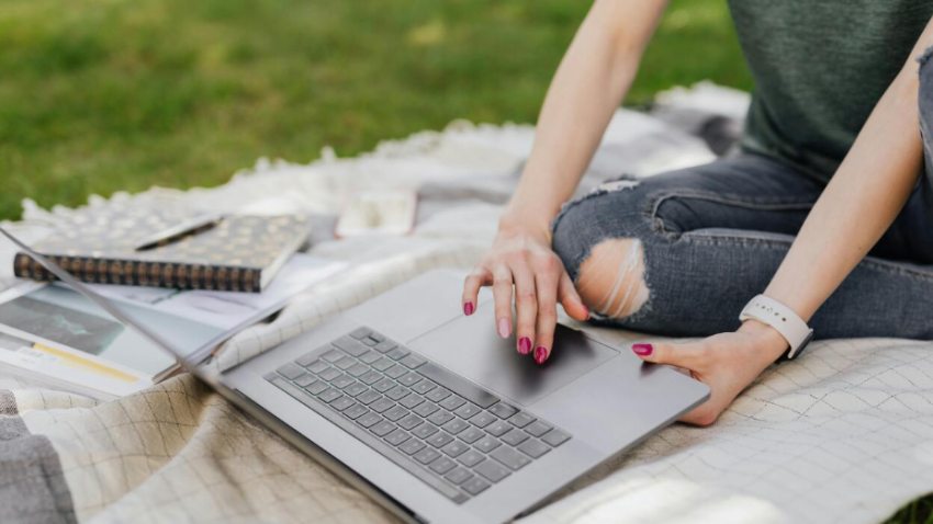 A person using a laptop on a blanket outside on grass