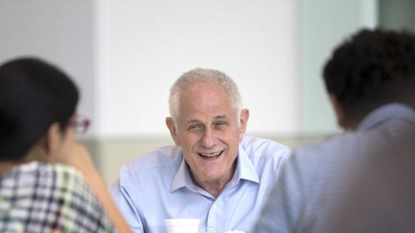 Zvi Galil in a light blue button-up shirt, seated and laughing