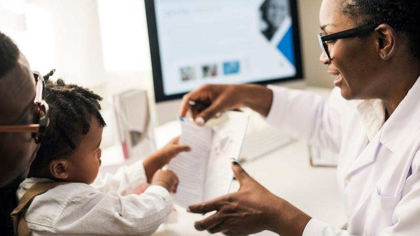 Doctor showing a pamphlet to a child who is seated on a parent's lap