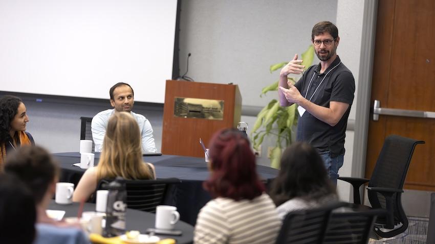 Mark Riedl standing up at a table speaking to others seated at tables