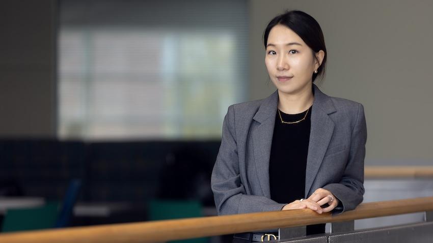 Asian woman in a black shirt and gray blazer standing at a railing inside a building