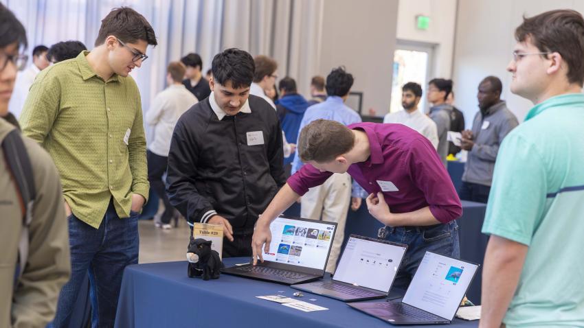 People standing around laptops that are on a table