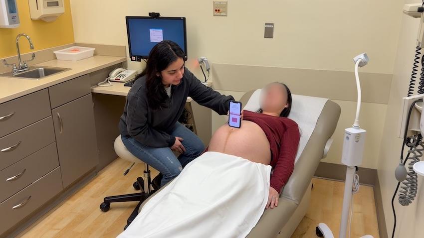 A medical professional holding a smartphone to a pregnant woman's belly in an exam room