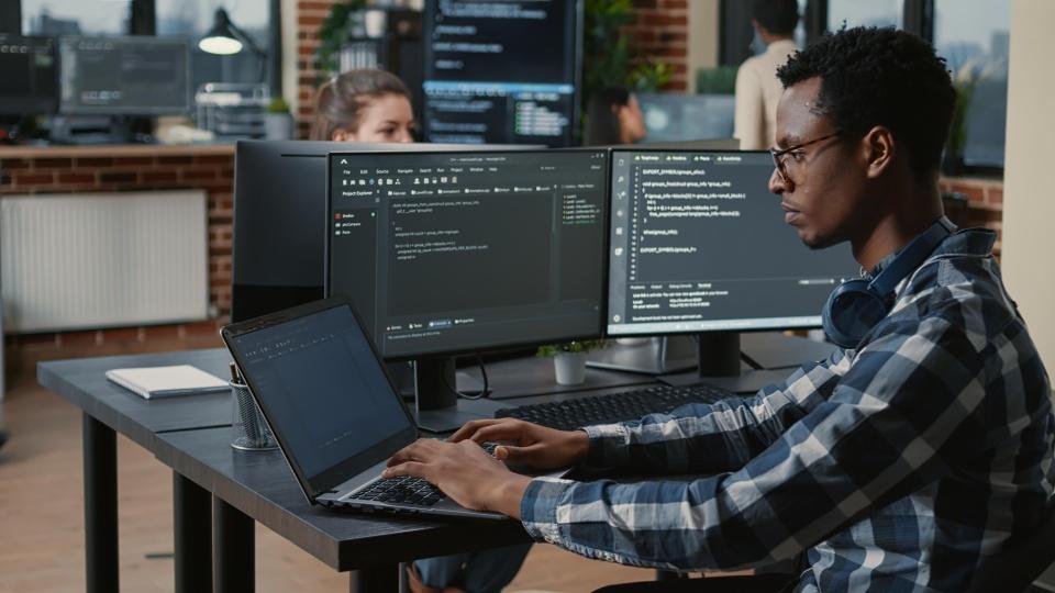 Man writing code on a laptop in an open office